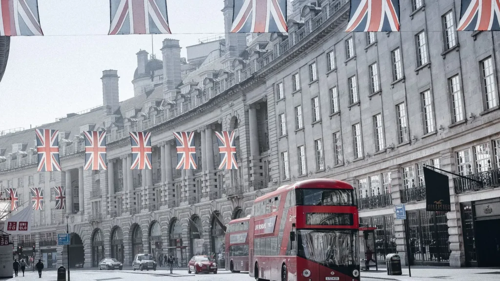 Červený dvoupatrový autobus na Regent Street v Londýně pod britskými vlajkami